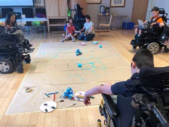 Campers sitting on the floor and using C2LC prototype on their laptops to code Dash and Sphero robots. Sphero is dipped in paint and markers are tapped to Dash, so they can draw shapes as they execute campers’ programs.